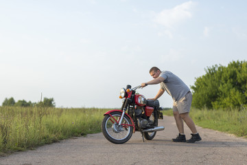 A man stands near motorcycle on a clear summer day