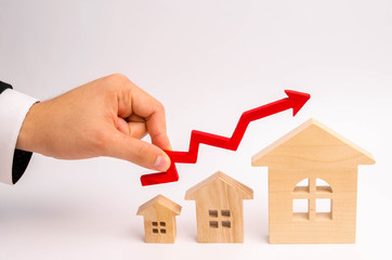 businessman's hand holds the red arrow up above the houses. The concept of growth in demand for...