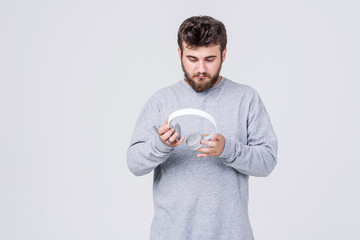 A young man in casual clothes is holding wireless headphones in his hands, studying their connection to a mobile phone