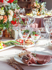 Table served for wedding banquet with cutlery and flowers in vases. Salads, appetizers and glasses with wine.
