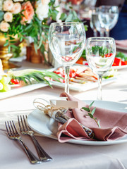 Table served for wedding banquet with cutlery and flowers in vases. Salads, appetizers and glasses with wine.