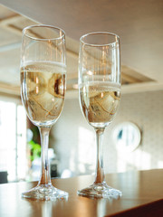 Pair of wine glasses with champagne. Beige room is reflected in a transparent glass of sparkling wine.