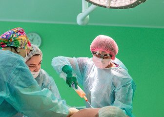 cosmetic liposuction surgery in actual operating room, group of surgeons working with cannula