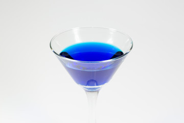 Halloween inspired blue color cocktail in a clear glass sitting on a white table waiting to be enjoyed.