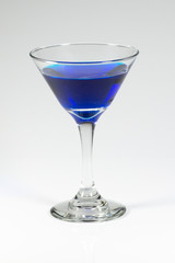 Halloween inspired blue color cocktail in a clear glass sitting on a white table waiting to be enjoyed.