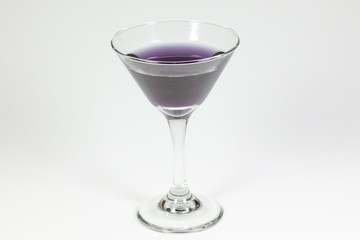 Halloween inspired purple color cocktail in a clear glass sitting on a white table waiting to be enjoyed.