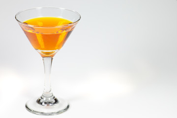 Halloween inspired orange color cocktail in a clear glass sitting on a white table waiting to be enjoyed.