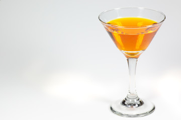 Halloween inspired orange color cocktail in a clear glass sitting on a white table waiting to be enjoyed.
