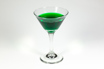 Halloween inspired green color cocktail in a clear glass sitting on a white table waiting to be enjoyed.