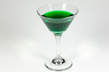 Halloween inspired green color cocktail in a clear glass sitting on a white table waiting to be enjoyed.