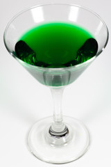Halloween inspired green color cocktail in a clear glass sitting on a white table waiting to be enjoyed.