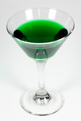 Halloween inspired green color cocktail in a clear glass sitting on a white table waiting to be enjoyed.