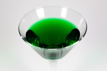 Halloween inspired green color cocktail in a clear glass sitting on a white table waiting to be enjoyed.