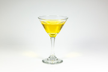 Halloween inspired yellow color cocktail in a clear glass sitting on a white table waiting to be enjoyed.