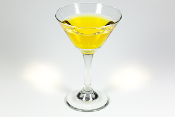 Halloween inspired yellow color cocktail in a clear glass sitting on a white table waiting to be enjoyed.