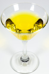 Halloween inspired yellow color cocktail in a clear glass sitting on a white table waiting to be enjoyed.