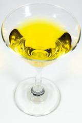 Halloween inspired yellow color cocktail in a clear glass sitting on a white table waiting to be enjoyed.