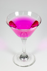 Halloween inspired Pink color cocktail in a clear glass sitting on a white table waiting to be enjoyed.