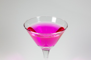 Halloween inspired Pink color cocktail in a clear glass sitting on a white table waiting to be enjoyed.