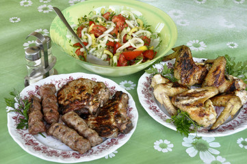steak and chevachchi with a grill in a bowl with parsley plate with grilled wings and a plate with salad one cucumber, tomato, onion.