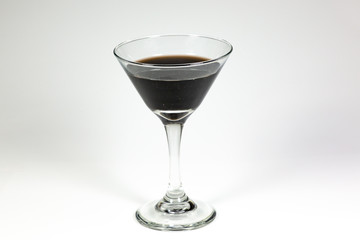 Halloween inspired black color cocktail in a clear glass sitting on a white table waiting to be enjoyed.