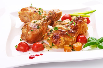 Roasted chicken legs with baked potatoes and vegetables, isolated on white background.