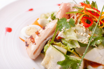 Caesar salad with quail eggs, cherry tomatoes, Parmesan cheese and grilled calamari, octopus in white plate on light table.