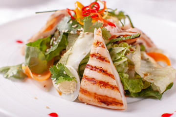 Caesar salad with quail eggs, cherry tomatoes, Parmesan cheese and grilled calamari, octopus in white plate on light table.