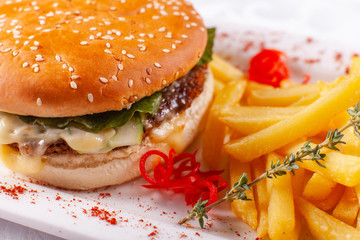 Fast food restaurant menu. Home made hamburger with the beef patties, onion, tomato, lettuce and cheese. Fresh burger close-up. Garnished with golden French fries potatoes