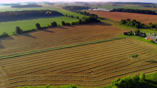 Colorful ultralight paraglider, parasail, flying above rural farms, early morning.
