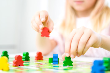 little blonde girl hold red people figure in hand. yellow, blue, green wood chips in children play - Board game and kids leisure concept