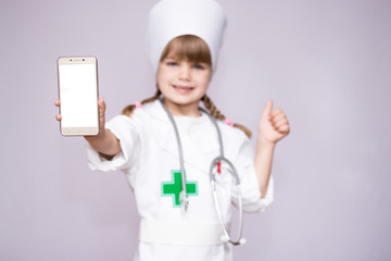 Smiling little girl in medical uniform holding smartphone with blank screen