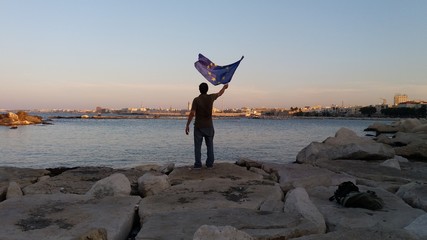 un uomo mentre fa sventolare la bandiera europea verso la città di Bari