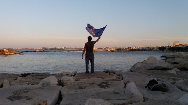un uomo mentre fa sventolare la bandiera europea verso la citt&agrave; di Bari