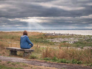 Fototapeta premium Woman sitting on a bench relaxing and enjoying beautiful seascape and clouds over ocean. 
