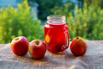 jar full of fruit juice with red apples on nature background