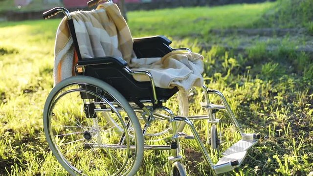 grey steel wheelchair outdoors in sunny summer green park with bright sun shining on background illness rehabilitation nobody body recovery transport for invalid pralysis medicine healthcare concept