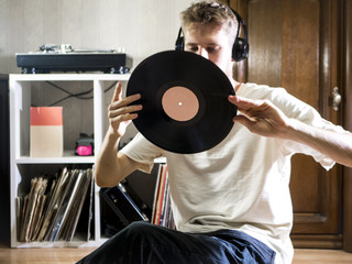 young man sitting in cozy living room holding the vinyl record disk near the records rack on the...