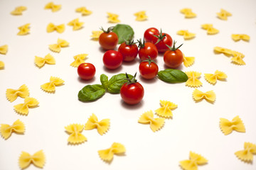 Isolated fresh red and orange cherry tomatoes with green leafs of basil and yellow pasta