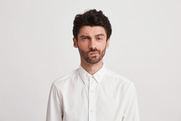 Closeup of serious displeased young businessman with bristle wears shirt looks pensive and dissatisfied isolated over white background