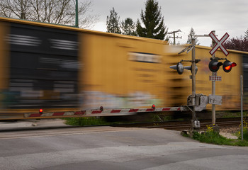Naklejka premium Street Level Railway Crossing. A train passes a level train crossing with the crossing arms down and lights flashing.