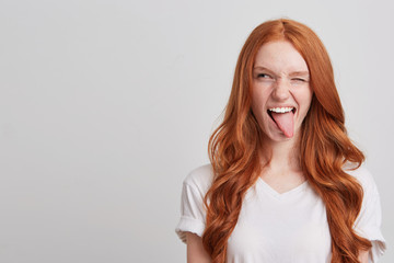 Portrait of cheerful playful young woman with long wavy red hair and freckles wears t shirt winks...
