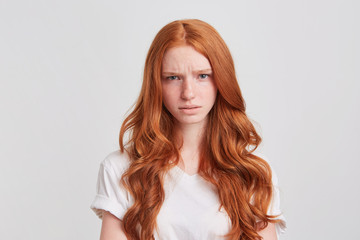 Closeup of unhappy worried redhead young woman with long wavy hair wears t shirt feels angry and...