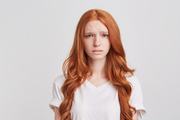 Closeup of depressed upset redhead young woman with long wavy hair wears t shirt feels desperate...