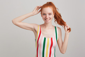 Closeup of cheerful lovely redhead young woman with freckles and ponytail wears striped top,...