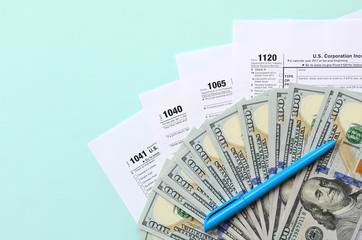 Tax forms lies near hundred dollar bills and blue pen on a light blue background. Income tax return