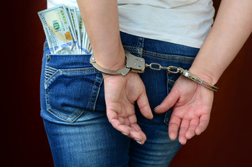 An arrested girl with handcuffed hands with a huge amount of dollar bills. Back view