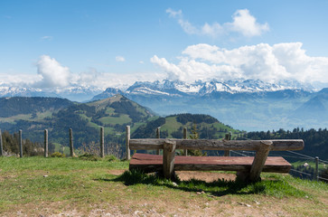 Brown wooden chair overlooking the swiss alps on mount rigi. Rest station with a view. Snow capped mountains