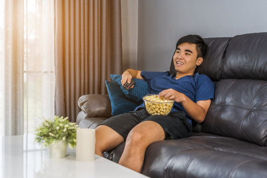 man eating popcorn while sitting on a couch at home and watching TV