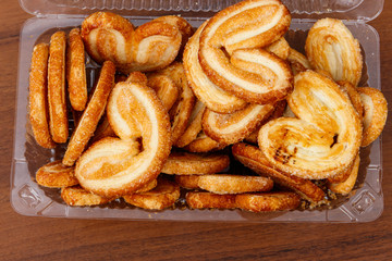 Palmier biscuits - french cookies made of puff pastry (also called palm leaves, elephant ears or french hearts) packed in plastic box on wooden table